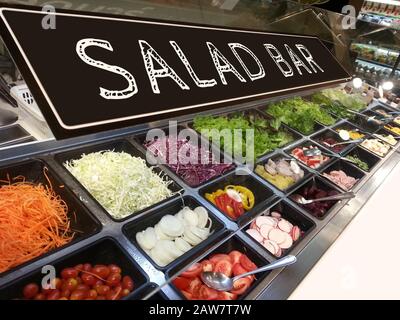 Verschiedene frische, bunte Gemüse- und Obstsorten an der Salatbar im Supermarkt mit einem Schild mit Salatbar Stockfoto