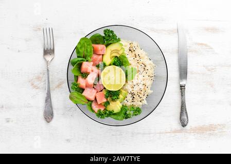 Reis mit Lachs, Avocado und Spinat. In einer schwarzen Platte auf Holzhintergrund Draufsicht. Freier Speicherplatz für Ihren Text. Flaches Lay Stockfoto