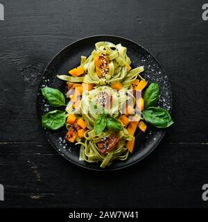 Pasta mit Kürbis und Spinat in einem schwarzen Teller auf schwarzem Grund. Draufsicht. Freier Speicherplatz für Ihren Text. Stockfoto