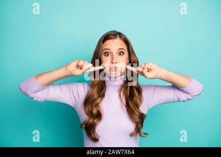 Closeup-Foto von lustiger gewellter Frisur Dame drückt die Finger Wangenknochen halten Atemzug kindliche Stimmung verrückt Gesicht tragen violetten Pullover Turtleneck isoliert Stockfoto