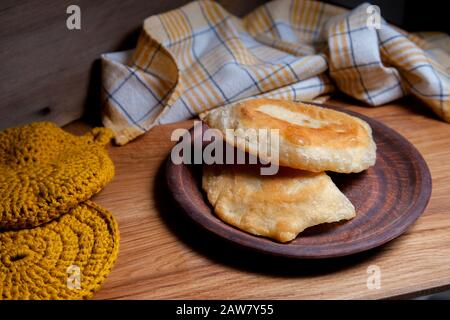 Tonplatte mit zwei einzelnen gebratenen Pasteten mit Fleisch auf Holztisch. Tatarische traditionelle Pasteten. Stockfoto