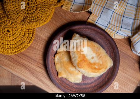 Tonplatte mit zwei einzelnen gebratenen Pasteten mit Fleisch auf Holztisch. Tatarische traditionelle Pasteten. Stockfoto