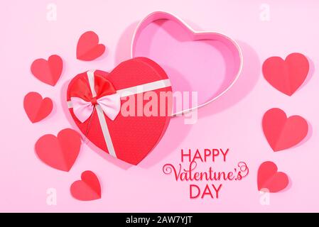 Beschreibung: Happy Valentines Day, Valentinstag Hintergrund mit schriftlicher Notiz, geöffneter Geschenkkasten in Herzform mit Band und kleinen Papierherzen, auf Stift Stockfoto
