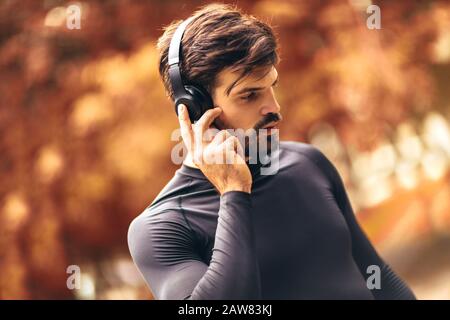 Portrait des jungen Mannes beim morgendlichen Joggen im Herbstpark, der mit Kopfhörern Musik hört Stockfoto
