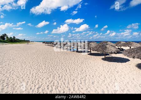 Breiter Sandstrand mit Sonnenliegen und Strohschirmen im Hintergrund des blauen Meeres Stockfoto