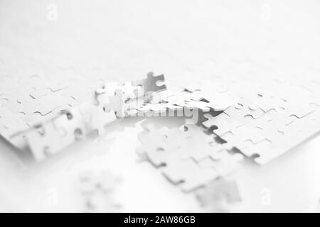 Auf einem weißen Tisch befindet sich ein weißes Puzzle, das auf einer Seite zerlegt oder in Stücke zerbrochen ist. Stockfoto