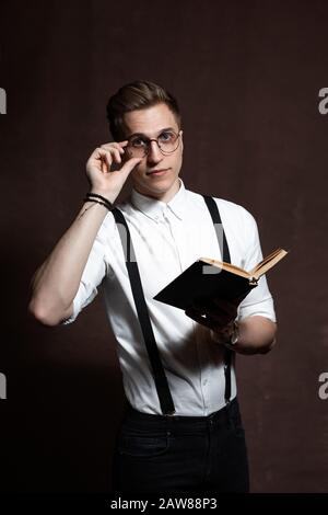 Eleganter junger Mann in runder Brille, Hosenträger, in einem weißen Hemd liest sich ein Buch Stockfoto