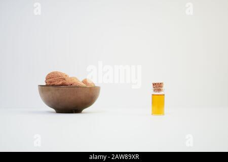 Walnüsse (Juglans Regia) in einer bronzefarbenen Schüssel und eine Probe Nussöl in einer Glasflasche auf weißem Grund Stockfoto