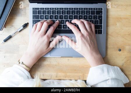 BirdsEye Draufsicht auf die weiblichen Hände, die auf einem Laptop auf einem Tisch schreiben. Stockfoto
