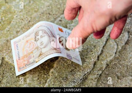 Ein glücklicher Rentner findet Geld auf dem Boden Hand reicht bis zu holen eine neue zehn Pfund Note Pfund vom Boden. England Großbritannien Stockfoto