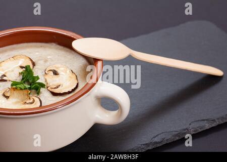 Hausgemachte Pilzsuppe in Porzellanschale mit Champignons in Scheiben auf schwarzem Steinbrett. Draufsicht. Stockfoto