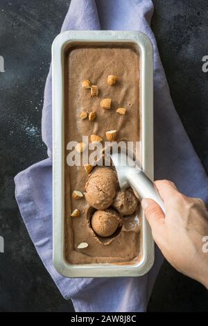 Frau stellt Bälle von Schokolade hausgemachtem Eis auf Schwarz her. Ansicht von oben. Sauberes Essen. Ohne Zucker. Stockfoto