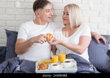 Guten Morgen. Gesundes Frühstück im Bett. Wunderschönes Liebes-Mittelpaar sitzt im Bett, bevor es frühstücken kann. Stockfoto