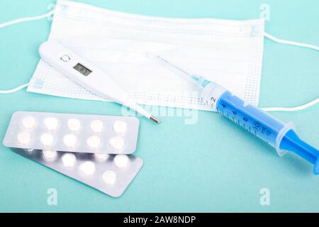 Kaltschutz medizinisches Zubehör auf blauem Hintergrund. Maskieren Sie Atemschutzthermometer, Pillen und Spritze. Stockfoto