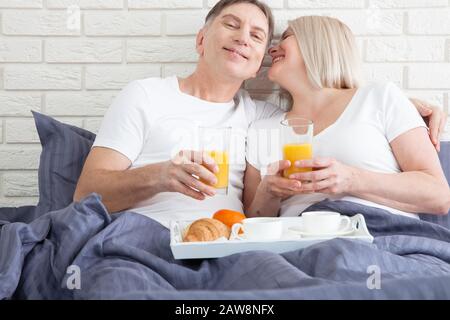 Guten Morgen. Gesundes Frühstück im Bett. Wunderschönes Liebes-Mittelpaar sitzt im Bett, bevor es frühstücken kann. Stockfoto