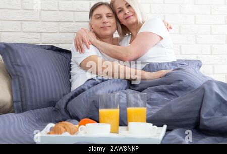 Guten Morgen. Gesundes Frühstück im Bett. Wunderschönes Liebes-Mittelpaar sitzt im Bett, bevor es frühstücken kann. Stockfoto