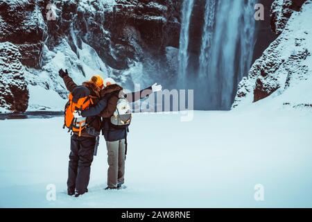 Glückliches Paar mit fantastischer Aussicht auf den Wasserfall Skogafoss, Spaß im Winter Reisen nach Island, aktive Winter-Flitterwochen Stockfoto