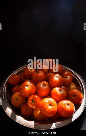 Frisch geerntete, reife rote Tomaten, die in einem rustikalen Stahlteller an einem sonnigen Ort in der Küche aufbewahrt werden. Tomaten für Sauce, Chutney, Ketchup, Marmelade. Stockfoto