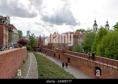 Peopl beim Spaziergang an den befestigten Ziegelmauern der Altstadt Warschaus mit Blick auf den Barbican-Turm Stockfoto