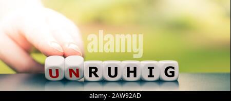 Hand dreht Würfel und ändert das deutsche Wort "unruhig" ("twitchy") in "ruhig" ("ruhig"). Stockfoto