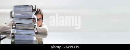 Nahaufnahme EINER Überarbeiteten Frau, Die Sich Hinter Dem Stapel von Ordnern Am Schreibtisch Am Arbeitsplatz Versteckt Stockfoto