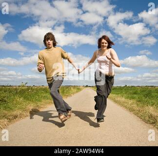 Ein Teenager-Paar hält die Hände und runterläuft eine Landspur in Richtung Kamera Stockfoto