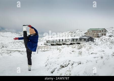 Frauen, die einen stehenden Yoga machen, spaltet sich im Schnee auf, mit Ben Lomond Ski-Resort Hintergrund, Tasmanien, Australien Stockfoto