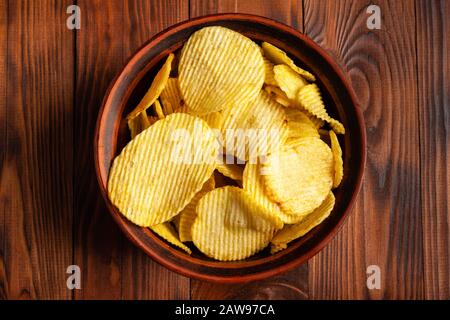 Wellenförmige Kartoffelchips in einem Teller auf einem Holztisch. Snacks von oben. Stock Fotopartoffel Chips mit leerem Platz. Stockfoto