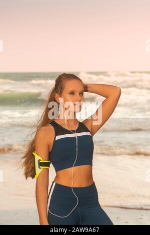 Fit für sportliche Frau mit Sportswear und einem Armband für Smartphone, am Meer stehend Stockfoto