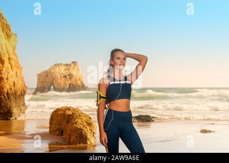 Fit für sportliche Frau mit Sportswear und einem Armband für Smartphone, am Meer stehend Stockfoto