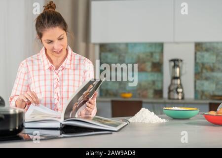 Fokussierte Frau prüft ein Kochbuch mit Interesse Stockfoto