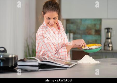 Frau, die eine Schüssel hält und ein Kochbuch prüft Stockfoto