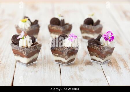 Schwarz-weiße Schokolade mit Plätzchen triflen. Dekoriert mit einer Blume auf altem weißen Holzhintergrund. Traditionelles süßes Dessert in englischer Sprache. Stockfoto