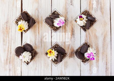 Schwarz-weiße Schokolade mit Plätzchen triflen. Dekoriert mit einer Blume auf altem weißen Holzhintergrund. Traditionelles süßes Dessert in englischer Sprache. Stockfoto