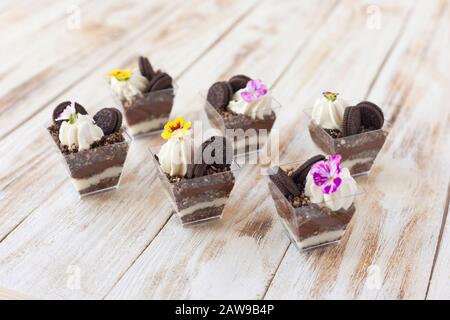 Schwarz-weiße Schokolade mit Plätzchen triflen. Dekoriert mit einer Blume auf altem weißen Holzhintergrund. Traditionelles süßes Dessert in englischer Sprache. Stockfoto