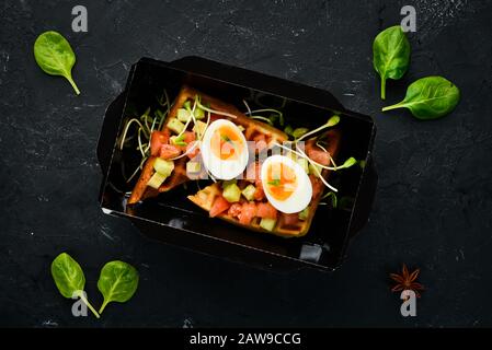 Herzhafte Waffeln mit Avocado, Tomaten und Ei. Lieferung von Lebensmitteln. Ernährungsgewohnheiten. Draufsicht. Freier Speicherplatz. Stockfoto