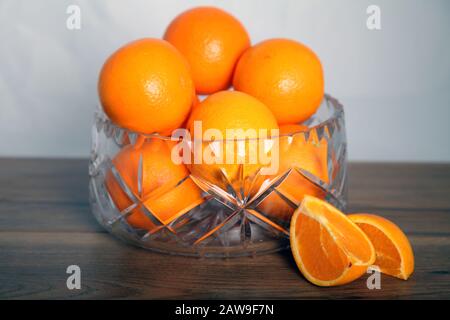 Bleikristall Obstschale voller Orangen 'Obst' gegen Weiß Hintergrund mit geschnittenen orangefarbenen Keilen Stockfoto