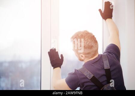 Der männliche Bauherr installiert und überprüft Kunststofffenster im Wohnhaus. Stockfoto