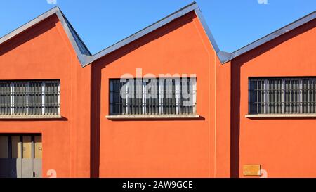 Altertümlicher Werkshall mit einer tief orangefarbenen Fassade an blauem Himmel, Zick-Zack-Dach und Fenstern in den südlichen Vorstädten Mailands, Italien Stockfoto