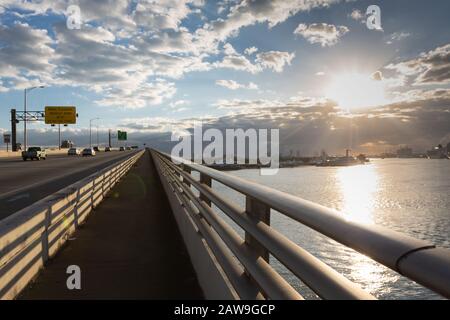 Fahrzeuge und Menschen, die den MacArthur Causeway bei Sonnenaufgang, Miami, Florida, USA überqueren Stockfoto