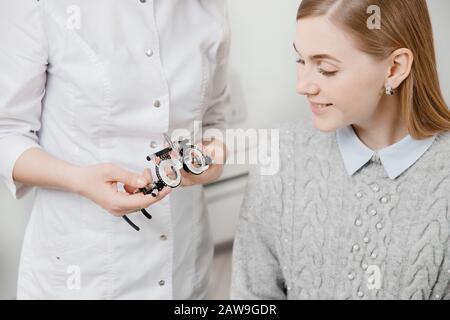 Junge schöne Patientin langhaarige Blondine mit jetzt weißem Lächeln, die eine spezielle Brille für die Auswahl der Linsen in der Hand sucht, Doktor weiße Robe. Pr Stockfoto