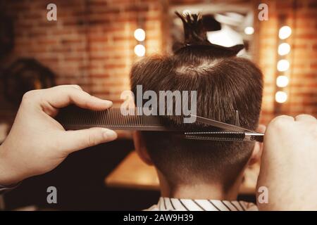 Junger Kerl mit Pferdeschwanz auf dem Kopf macht Haarschnitt in Männer Friseursalon barber Shop Stockfoto