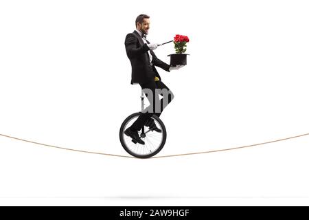 Zauberer mit einem Zauberstab, der auf einem Einrad reitet und einen Trick mit roten Rosen und einem Hut ausführt, der auf weißem Hintergrund isoliert ist Stockfoto