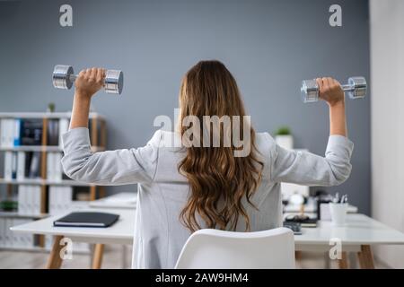 Lächelnde Junge Geschäftsfrau, Die Mit Fitness-Hanteln Im Büro Sport Macht Stockfoto