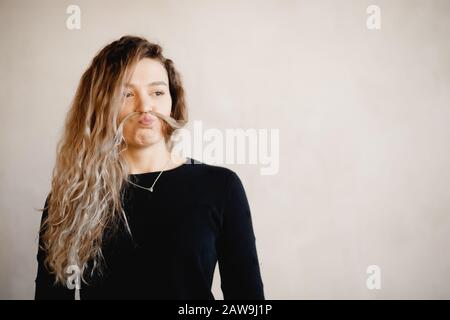 Portrait verspielte, windige Frau in schwarzer Jacke, die ihr ein Haarschloß wie einen Schnurrbart ins Gesicht legt Stockfoto