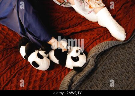 Nahaufnahme Der Füße Von Frauen in Haustierschuhen Form von Pandas aus Tier und warm weiche weiße Socken auf der Strickdecke Stockfoto