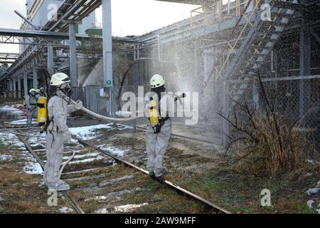 Rettungskräfte in schützenden Gummianzügen bewässern Pflanzengebiet mit Spritze. Schulung des Rettungsteams in der Dekontamination Stockfoto