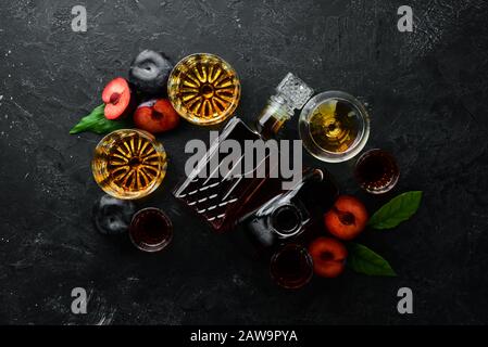 Slivovica - Pflaumenwodka, Pflaumenbrand in einer Flasche auf einem schwarzen Steintisch. Brille mit alkoholischen Getränken. Draufsicht. Freier Speicherplatz für Ihren Text. Stockfoto