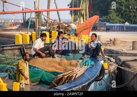 DIU, Indien - Dezember 2018: Fischer im Leerlauf und plaudern auf einem bunten Boot am Pier auf der Insel Diu. Stockfoto