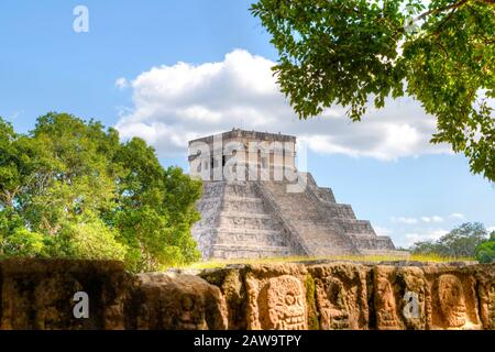 Die jahrhundertealte Plattform Tzompantli oder Wall of Skulls in Chichen Itza, Yucatan, Mexiko, mit der Kukulkan-Pyramide im Hintergrund. Die Plattform wurde t verwendet Stockfoto